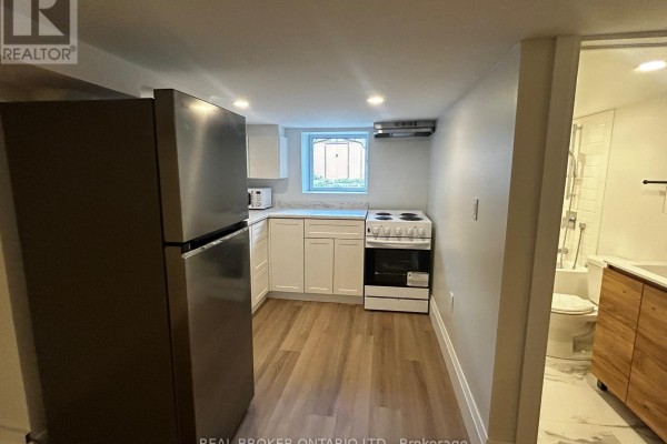 A compact kitchen with white cabinets, granite countertops, a black sink, and stainless steel refrigerator. - 3 - 659 Vaughan Road, Toronto