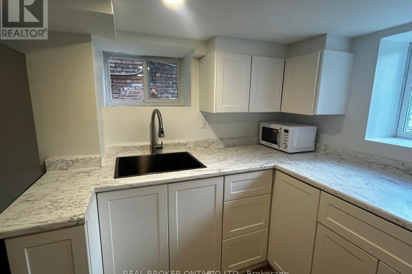 A small kitchen with white cabinets, granite countertops, a black sink, and two windows. - 3 - 659 Vaughan Road, Toronto