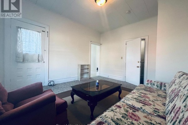 Living room with floral sofa, armchair, dark wood coffee table, and doors. - 3 - 80 Bridge Street W, Belleville