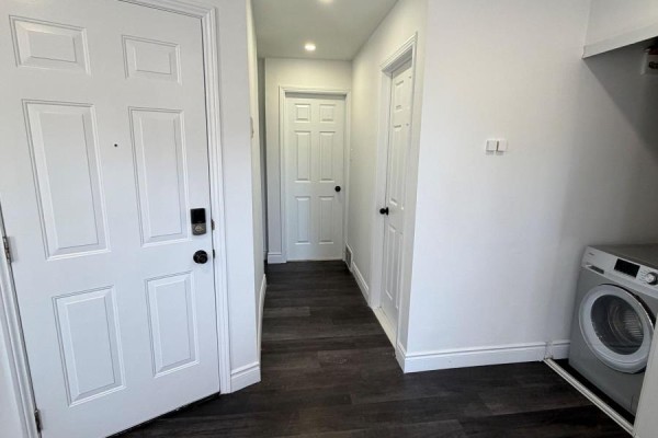 Interior hallway with dark wood-look flooring, white doors, and a washing machine. - 3 - 85 Wilson Street, Hamilton