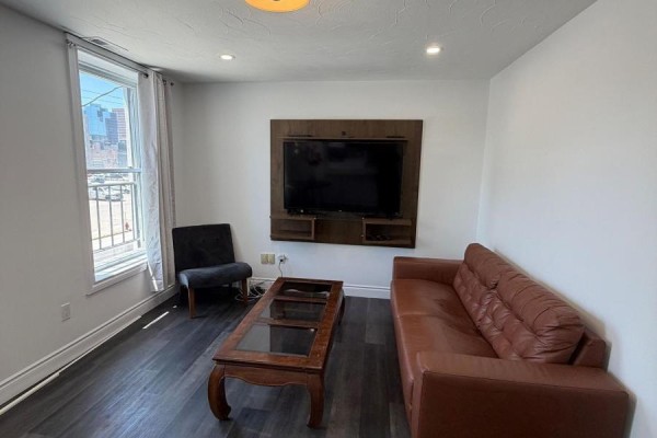 Living room with brown leather sofa, armchair, coffee table, and wall-mounted TV. - 3 - 85 Wilson Street, Hamilton