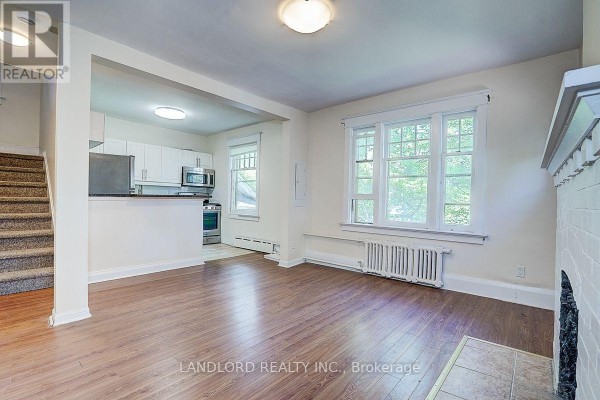 Living room with fireplace and windows, opening to a kitchen area. - 3 - 92 Neville Park Boulevard, Toronto