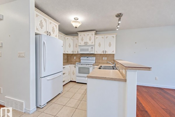 Corner kitchen with white cabinets, stainless steel appliances, and a beige countertop. - #3 10 Woodcrest Ln, Fort Saskatchewan