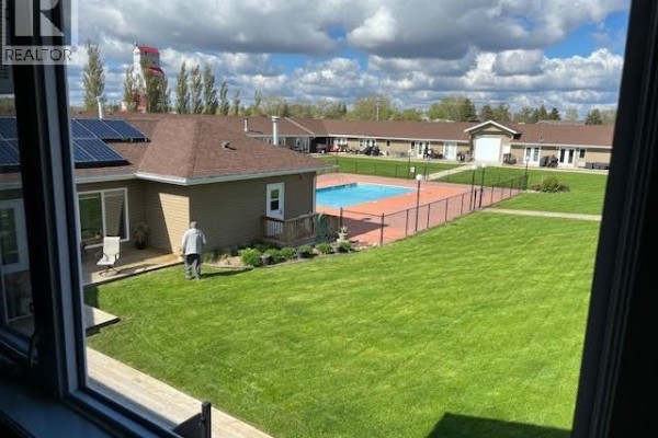 View from a window looking out at a green lawn, fenced swimming pool, and apartment buildings. - 3 1250 Aaro Avenue, Elbow