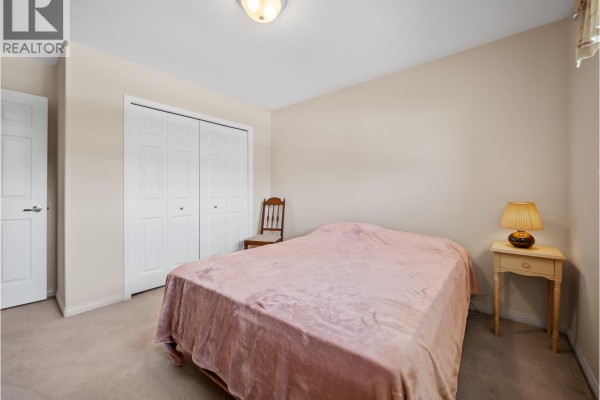 Bedroom with a large bed, pink blanket, beige carpet, and a wooden chair. - 3 1370 Riverwood Gate, Port Coquitlam