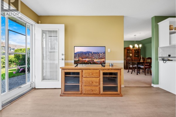 Living area with a TV on a wooden stand, a glass door, and a dining area beyond. - 3 1370 Riverwood Gate, Port Coquitlam