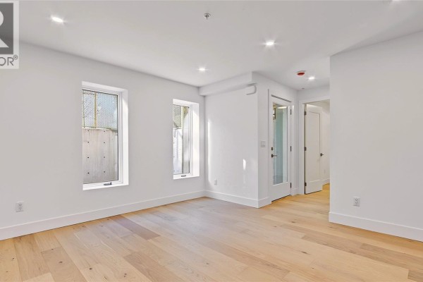 Living area with white walls, light wood floors, and two small windows looking out. - 3 1721 Adanac St, Victoria