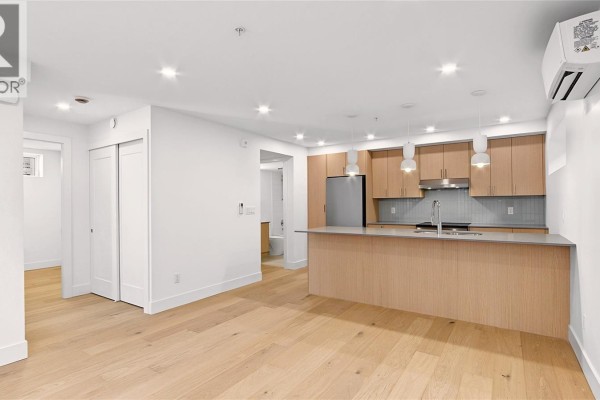 Living and kitchen area with light wood floors, white walls, and a kitchen island. - 3 1721 Adanac St, Victoria