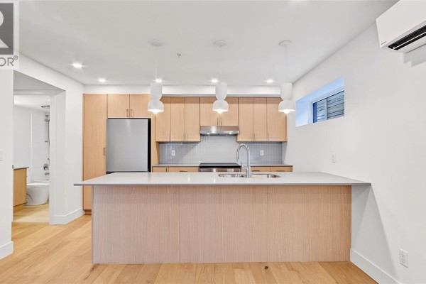 Kitchen with light wood cabinets, stainless steel appliances, and a large island with a sink. - 3 1721 Adanac St, Victoria