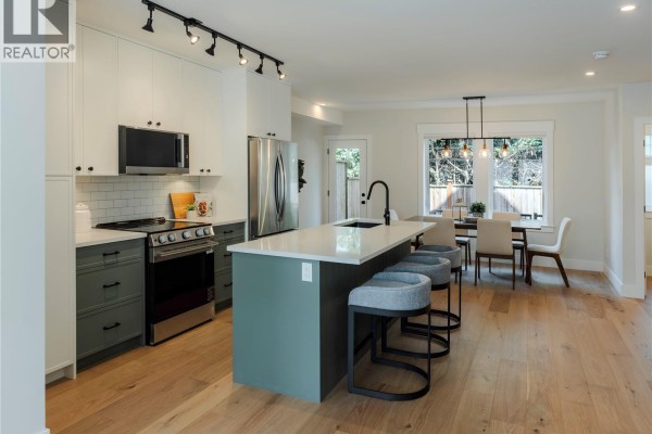 Dining table with chairs, kitchen island, and view of the living area and staircase. - 3 1830 Allenby St, Saanich