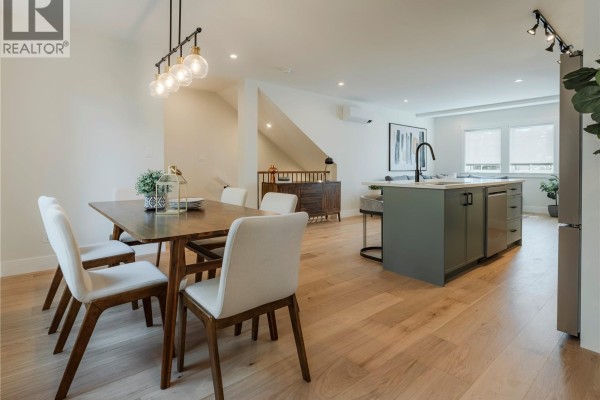 Wooden dining table with upholstered chairs and view of the backyard through double windows. - 3 1830 Allenby St, Saanich