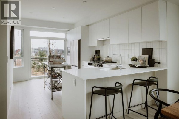 Kitchen with white cabinetry, island with bar seating, and stainless steel appliances. - 3 4552 Cattail Way, Tsawwassen