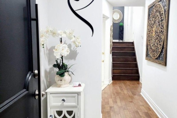 Entranceway of a house with a black door, white end table with flowers, and view of stairs. - 3 Blackthorn Lane E, Brampton