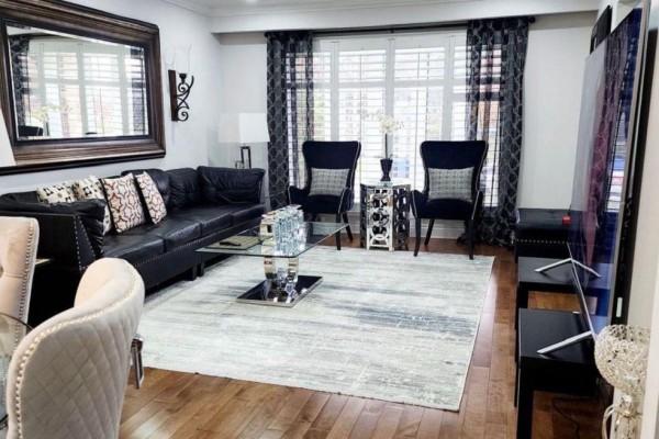 Living room with a black leather sofa, armchairs, glass coffee table, and large window. - 3 Blackthorn Lane E, Brampton