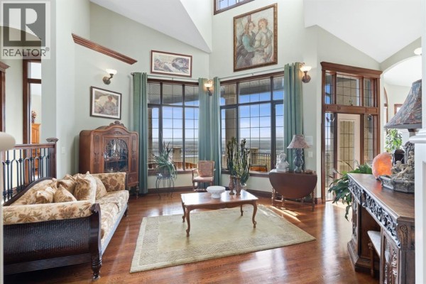 Living room facing the windows, showing a couch, coffee table, and large antique cabinet. - 3 Blackwell Bay, Rural Rocky View County