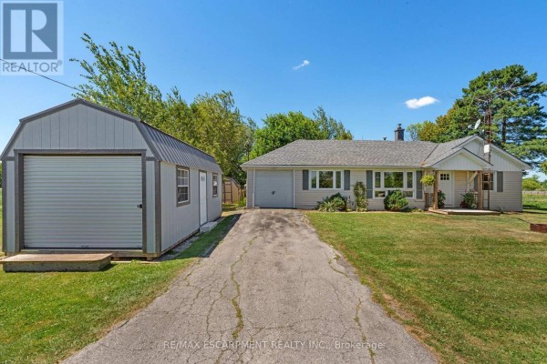 View of the beige bungalow and detached grey shed from the end of the cracked asphalt driveway. - 3 Bousfield Lane, Haldimand