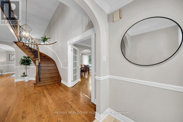 Interior foyer with hardwood floors, a curved staircase with dark banisters, and an arched opening to a dining area. - 3 Castlehill Road, Vaughan