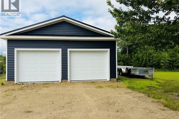 Front view of a dark blue detached garage with two white overhead doors and a trailer. - 3 Ch Manuel, Baie Sainte Anne