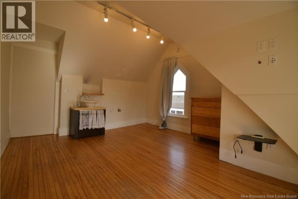 Attic room with sloped ceiling, wood floors, a small sink, and chest of drawers. - 3 Cross Unit# E, Moncton