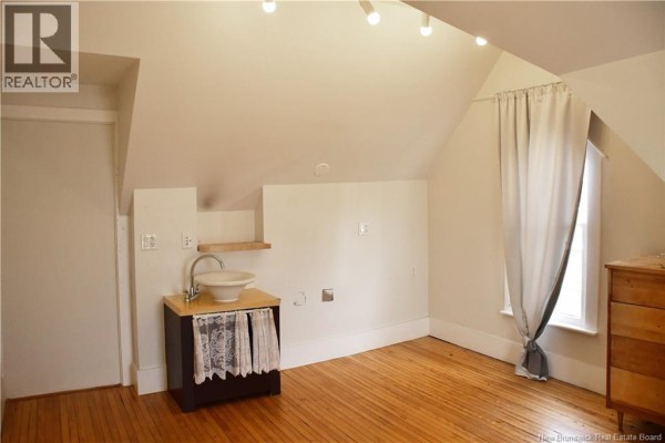 Attic room with slanted ceiling, wooden floor, small sink, and window with curtain. - 3 Cross Unit# F, Moncton