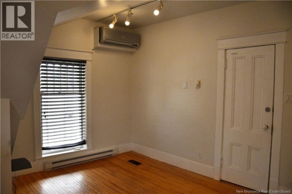 Room with sloped ceiling, wooden floor, window with blinds, and white door. - 3 Cross Unit# F, Moncton