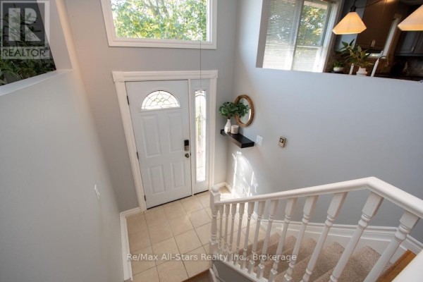 Interior view of a bright foyer with a front door, stairs, and beige tile flooring. - 4 Daniel Court, Kawartha Lakes
