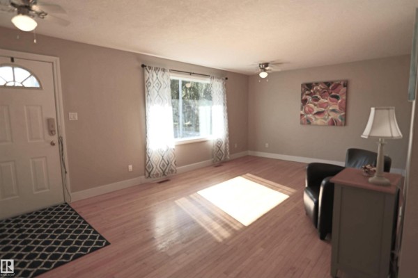 Living room with hardwood floors, beige walls, and a large window with patterned curtains. - 3 Dorchester Rd, Spruce Grove