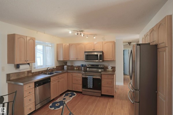 Corner view of the kitchen with light wood cabinets, stainless steel sink, dishwasher, and stainless steel refrigerator. - 3 Dorchester Rd, Spruce Grove