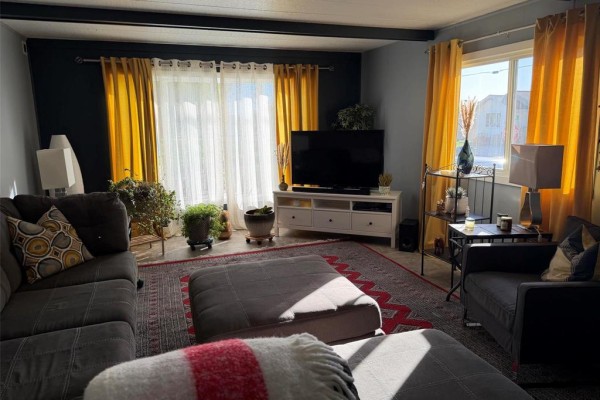 Living room with a grey sectional sofa, ottoman, yellow curtains, and television. - 3 Dray Place Sw, Altona