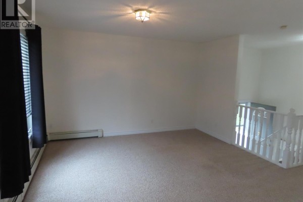 Empty living room with beige carpeting, white walls, black curtains, and a white railing staircase. - 3 Elmwood Ave, Sault Ste  Marie