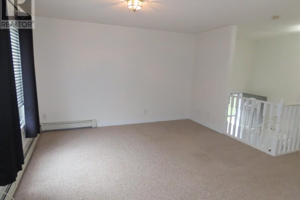 Spacious empty living room with beige carpeting, off-white walls, and a view of a staircase. - 3 Elmwood Ave, Sault Ste  Marie