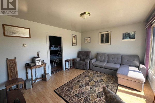 View of living room showing a sofa, armchair, doorway to a room with bunk beds, and wood flooring. - 3 Falcon Drive, Manitouwadge