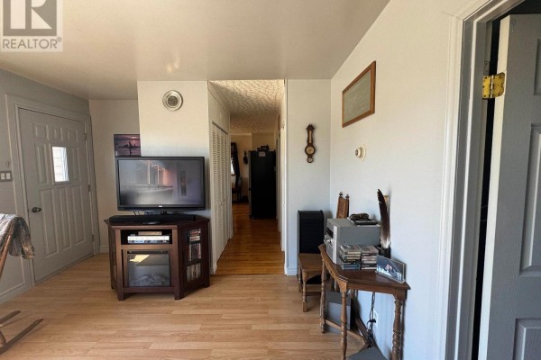 Living room area with a television, wood entertainment unit, and a hallway leading further into the house. - 3 Falcon Drive, Manitouwadge