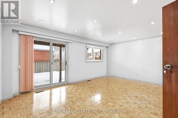 A spacious room with light gray walls, parquet flooring, a sliding glass door to the backyard, and a small window. - 3 Forest Point Drive, Toronto