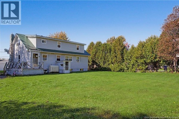 Rear view of a light grey multi-family house with a green roof, deck, and grassy yard. - 3 Gorman Boulevard, Miramichi