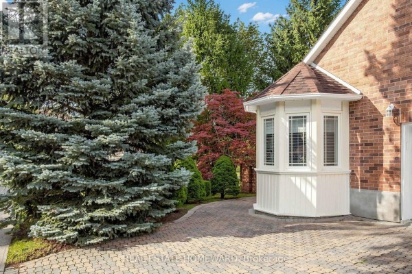 A detailed view of a white bay window on a brick house, with mature trees and shrubs. - 3 Green Acres Road, Vaughan