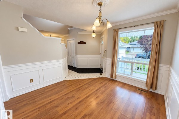 Empty dining room interior with wood laminate flooring, white wainscoting, and view of staircase. - 3 Hardcastle Pl, St  Albert