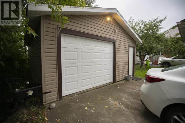 Single-car garage with a white overhead door, tan siding, and adjacent to a driveway. - 3 Henrietta Ave, Sault Ste  Marie