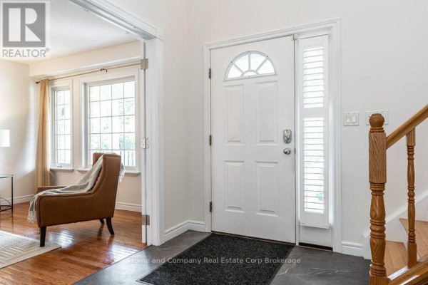 Interior front entrance with white door, arched window, hardwood stairs, and view into living room. - 3 Lightbourne Avenue, Stratford