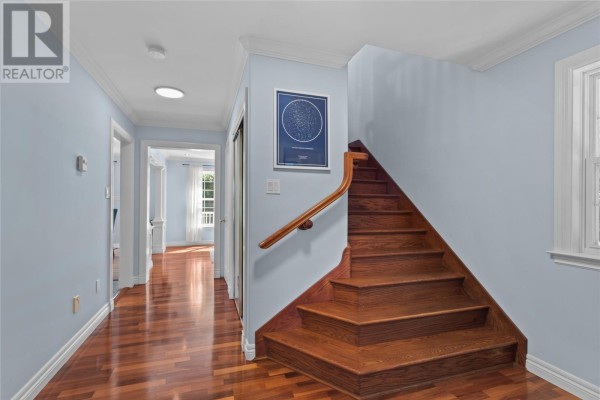 Hallway with light blue walls, wood floors, and a wooden staircase leading upstairs. - 3 Maple Street, Conception Bay South