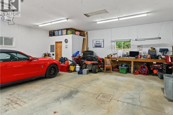 Interior of a spacious garage with a red car, riding mower, workbench, storage shelves, and various tools and equipment. - 3 Maple Street, Lower Woodstock
