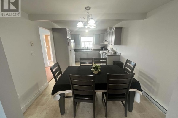 Dining area with a black tablecloth on a table, facing a grey kitchen with appliances. - 3 Mcgregor Lane, Wabush