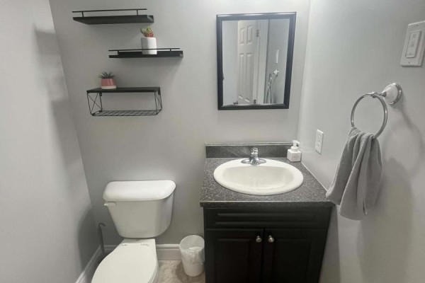 Small bathroom with a white toilet, a dark vanity, and a white sink with a mirror. - 3 Mcgregor Lane, Wabush