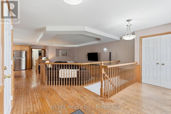Open concept living area with a sunken living room, wooden staircase, and stainless steel refrigerator. - 3 Ormond Street N, Thorold