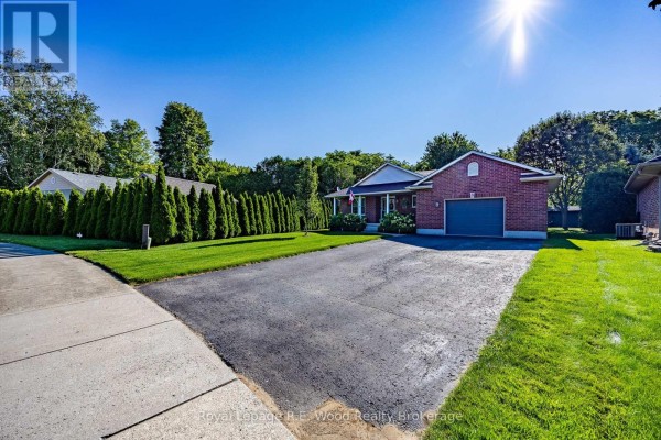 Side view of the brick bungalow showing the driveway, lawn, and mature trees. - 3 Otterview Drive, Norwich