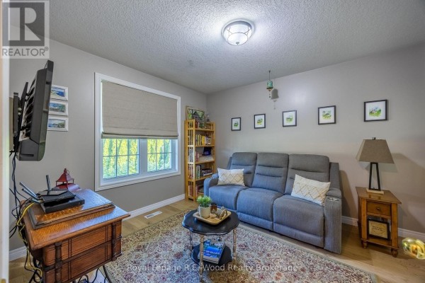 Living room with a grey sofa, patterned rug, television, and a window with green views. - 3 Otterview Drive, Norwich