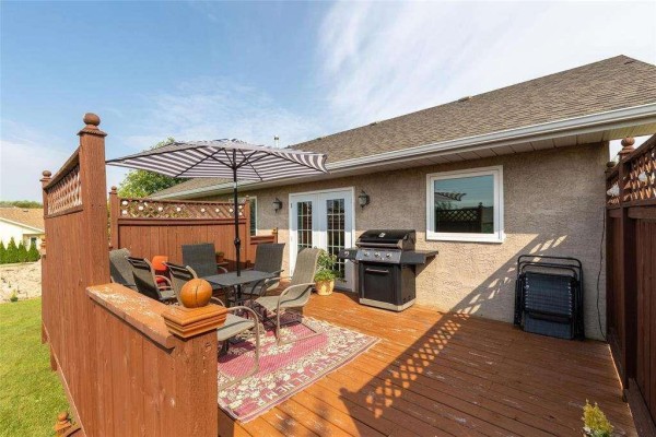 Wooden deck with outdoor dining set, grill, and umbrella in a fenced backyard. - 3 Parkwood Cove, Steinbach