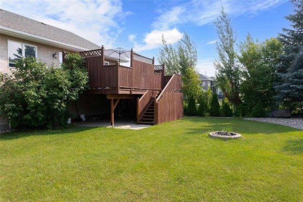 Backyard view featuring a raised wooden deck and fire pit area on a grassy lawn. - 3 Parkwood Cove, Steinbach