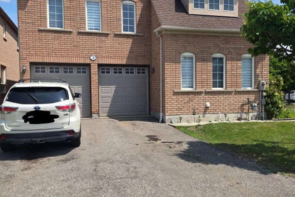 Exterior view showing a double-car garage and driveway of a brick townhouse. - 3 Wainwright Drive, Ajax