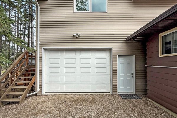 Gravel driveway with a white garage door, man door, and wooden stairs. - 3 White Spruce Crescent, Candle Lake